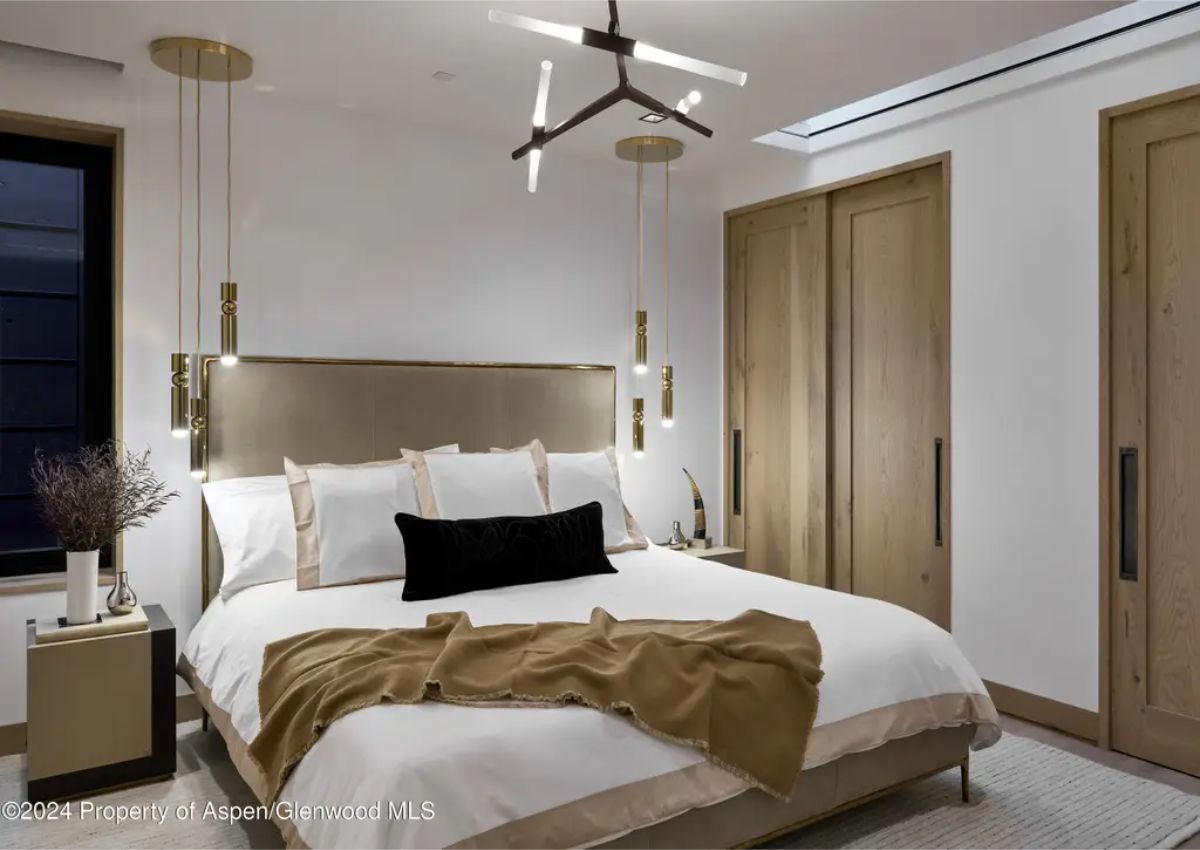 Luxurious bedroom presents a minimalist design, a plush bed, golden pendant lights, and a modern chandelier. 