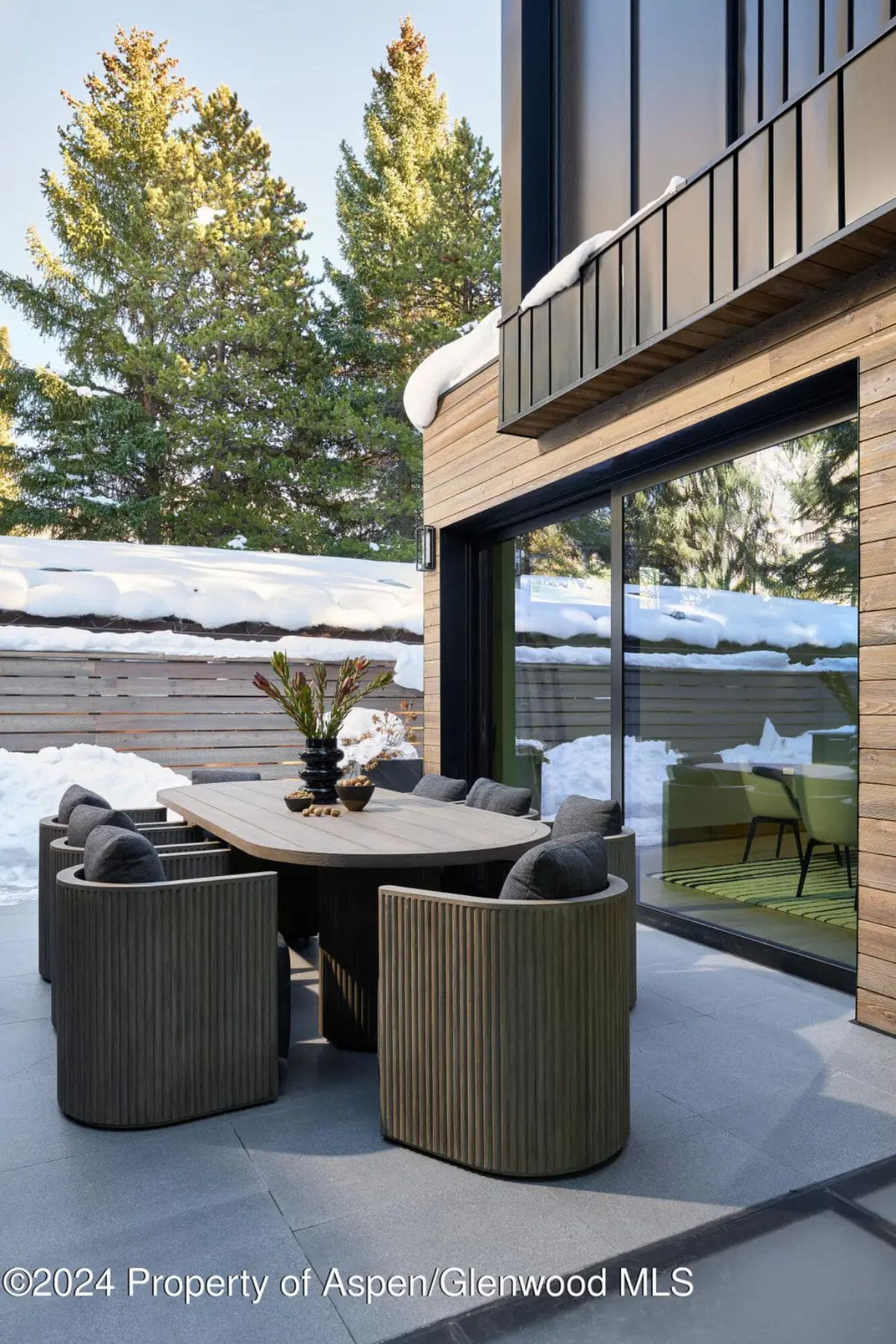 Outdoor dining area features a stylish wooden table, cushioned chairs, and a modern design surrounded by snow-covered scenery. 