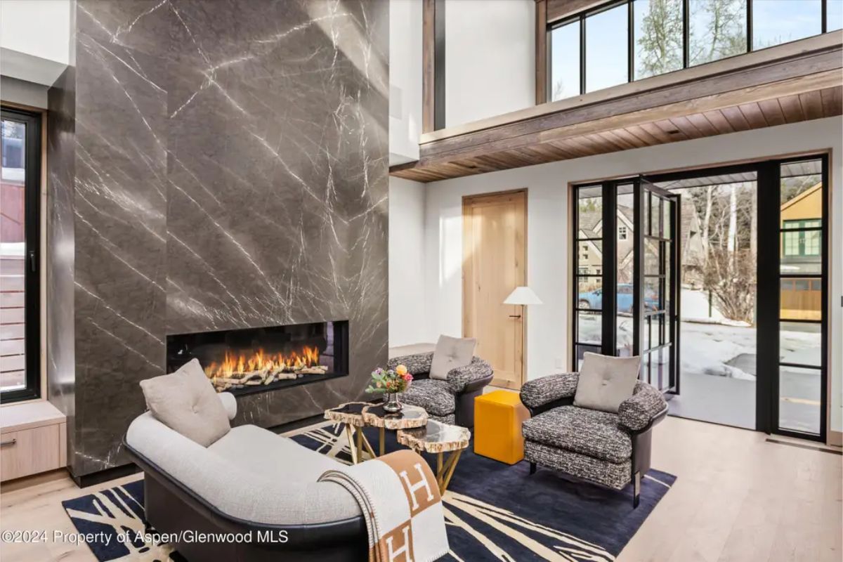 Elegant lounge space with a large marble accent wall, a fireplace, and doors leading to an outdoor winter landscape. 