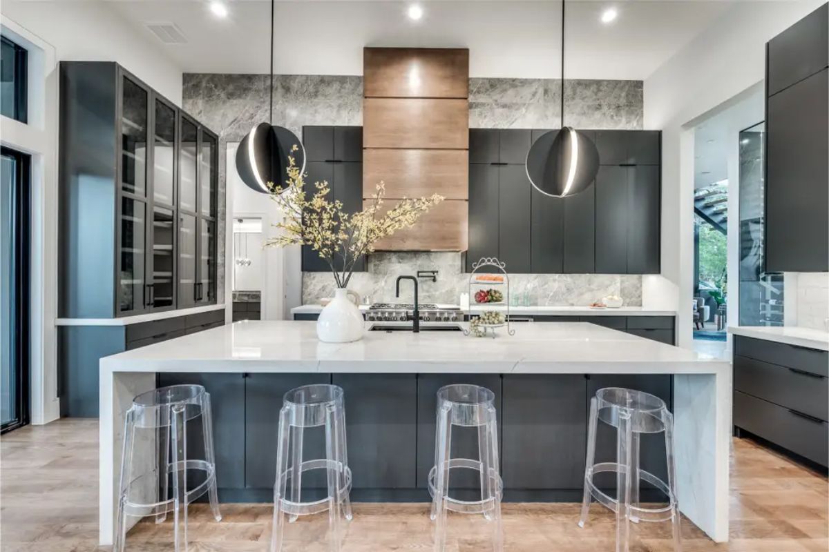 Kitchen features a sleek white marble island with transparent barstools and bold pendant lighting. 