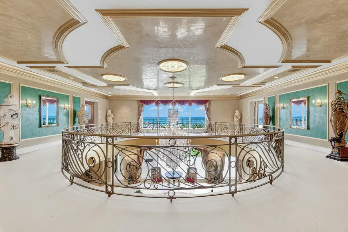 Upper-level gallery offers a breathtaking view of the chandelier below, accented by detailed ceiling molding and ocean-facing windows. 