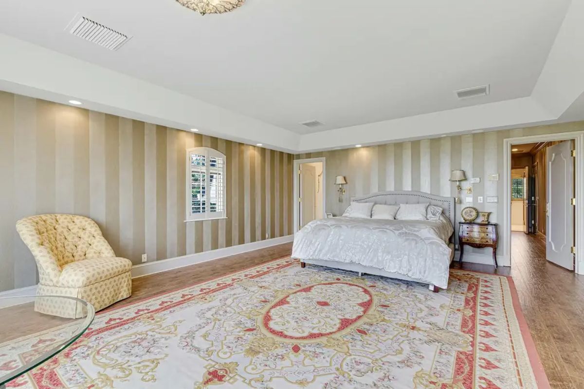 Master bedroom highlights striped wallpaper, plush carpeting, and classic furnishings for a refined, cozy atmosphere. 