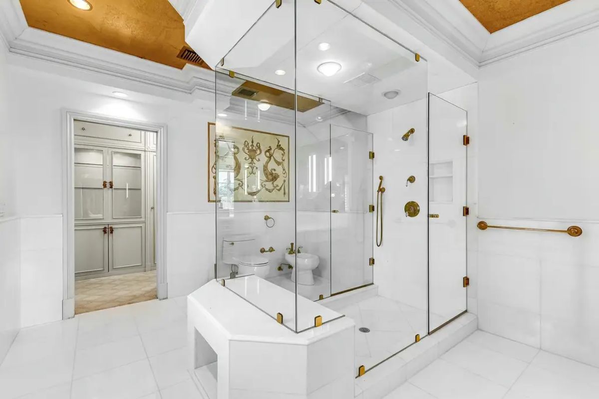 Luxurious bathroom boasts a glass-enclosed shower, white marble finishes, and gold accents for a sophisticated look. 