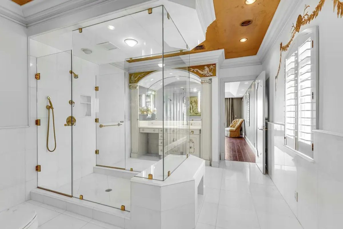 Luxurious bathroom highlights a large glass-enclosed shower with gold fixtures and a white vanity adorned with ornate details. 