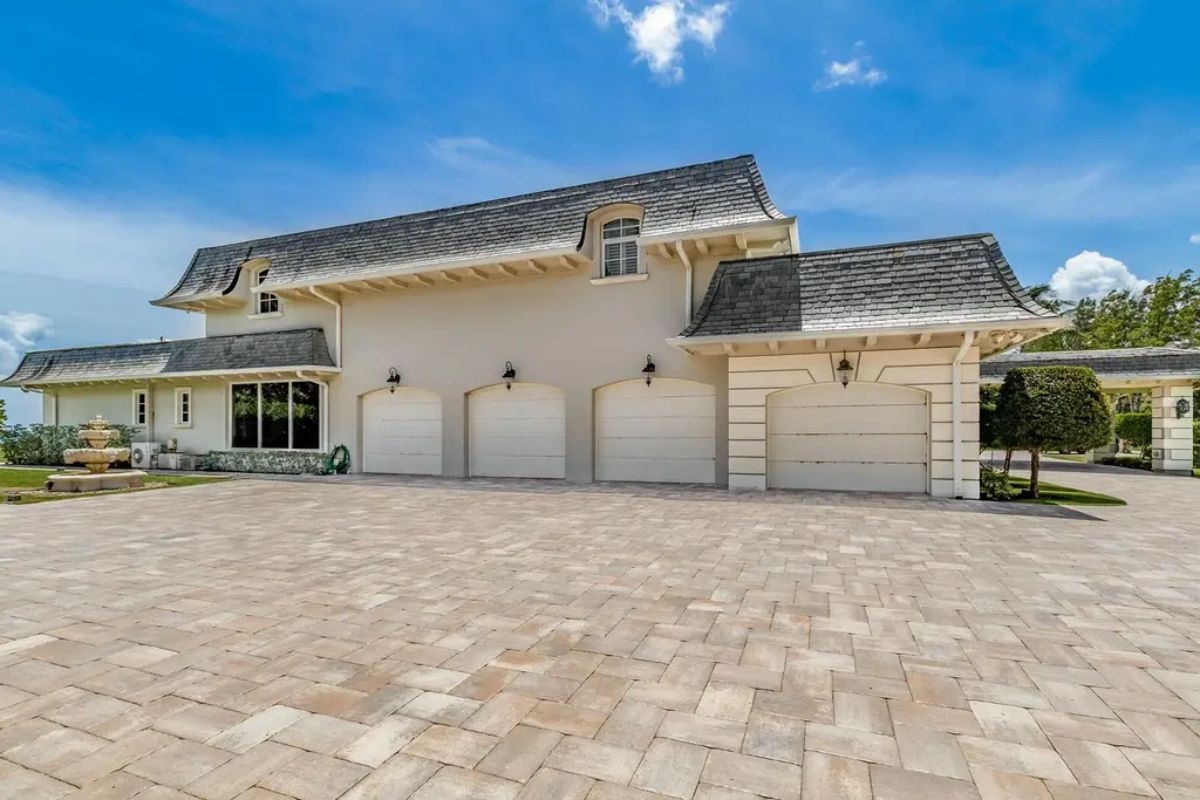 Grand garage area boasts multiple doors and a wide paved driveway, framed by neatly trimmed landscaping. 