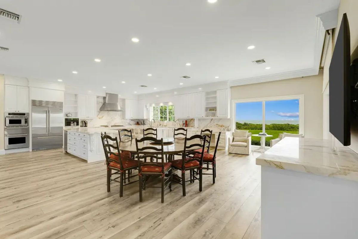 Spacious kitchen combines modern appliances, white cabinetry, and marble countertops with a cozy breakfast nook overlooking the greenery. 