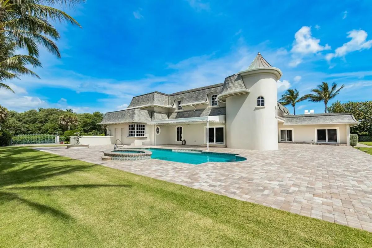 Expansive backyard view reveals a crystal-clear pool, manicured lawn, and elegant, castle-inspired home design. 