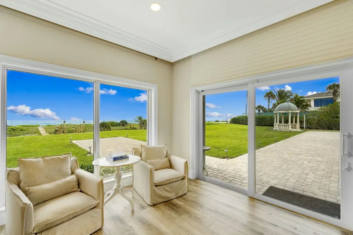 Inviting sunroom offers comfortable seating with expansive windows and sliding doors that open to lush greenery. 