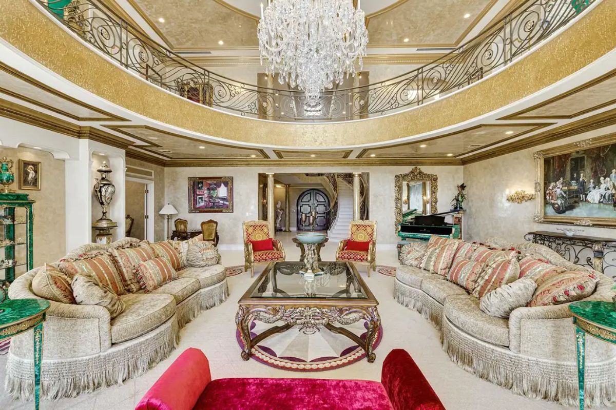 Lavish living room dazzles with plush seating, ornate furnishings, a crystal chandelier, and a balcony view from the upper level. 