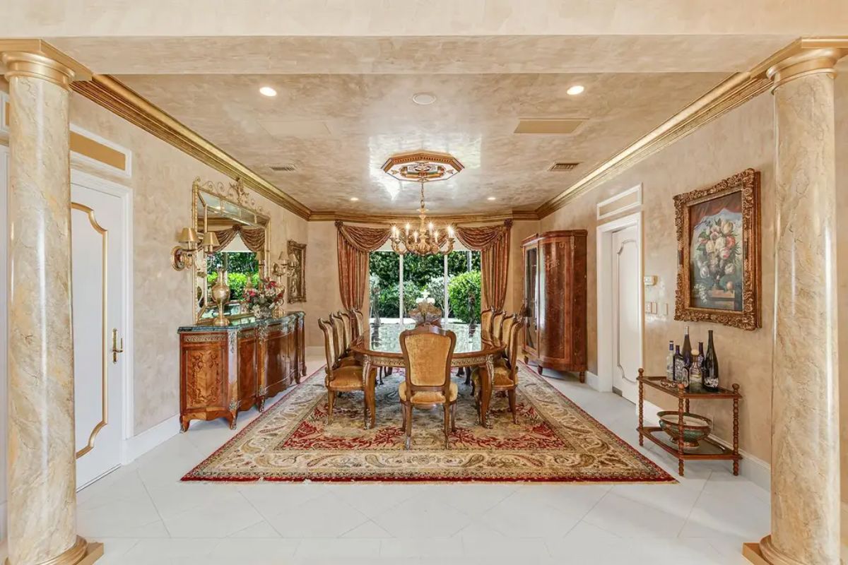 Formal dining room is adorned with rich wooden furniture, a crystal chandelier, and an elaborate patterned rug. 