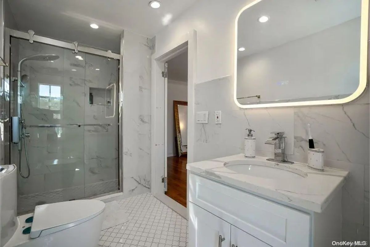 Walk-in shower with a glass enclosure features a rain-style showerhead and built-in shelving.