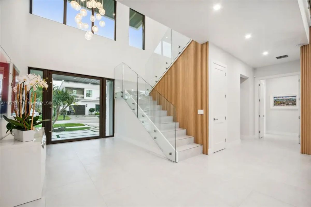 Spacious foyer with a grand staircase that has glass railings, a high ceiling, and a large chandelier. 
