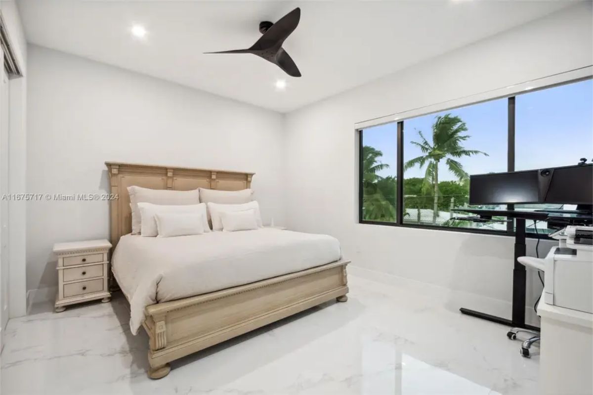 Elegant master bedroom with a wooden bed frame, large windows, and a home office corner. 