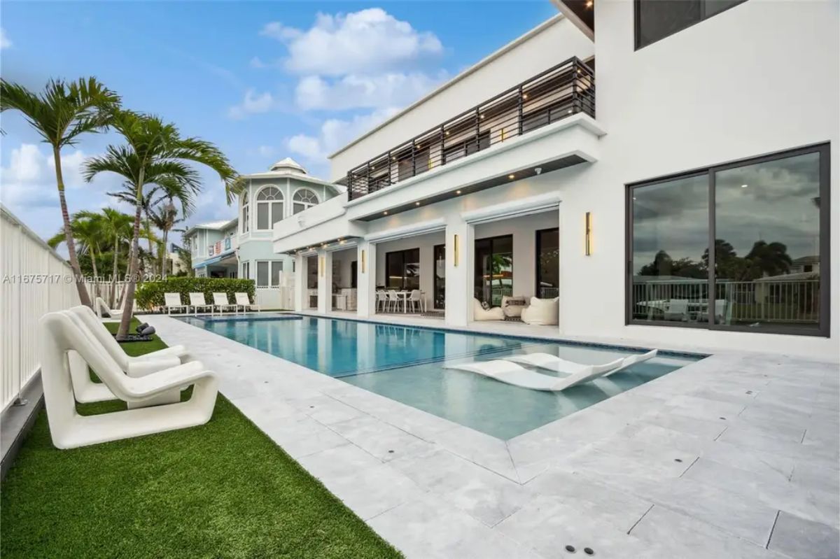 A modern two-story home features a sleek outdoor pool area with palm trees and a spacious patio. 