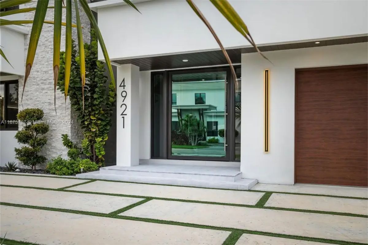 Close-up of the house entrance, featuring a sleek glass door, modern house number "4921," and elegant outdoor lighting. 