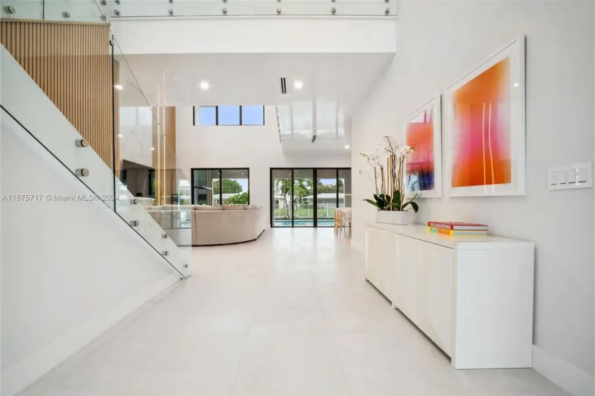 Hallway with white walls, modern artwork, and a console table with decorative elements leading to a bright living area. 