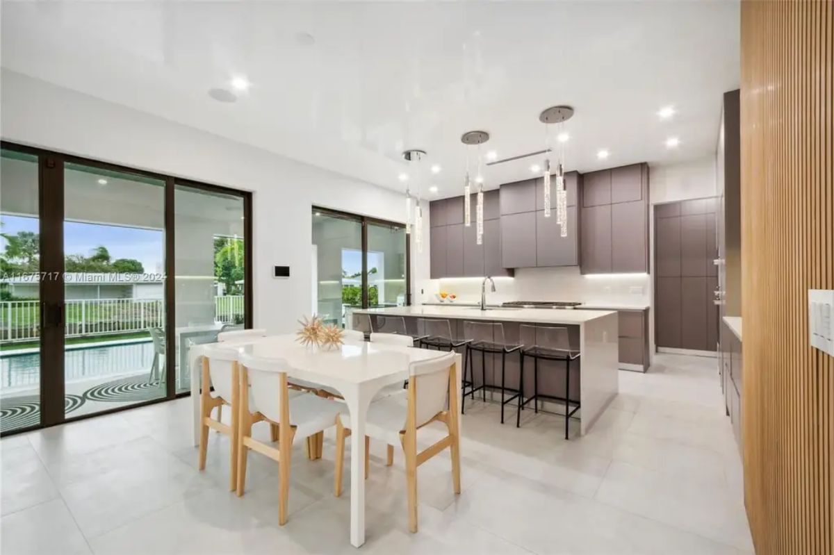 Modern kitchen and dining area with sleek cabinetry, a large island, and hanging pendant lights, seamlessly opening to the poolside patio. 