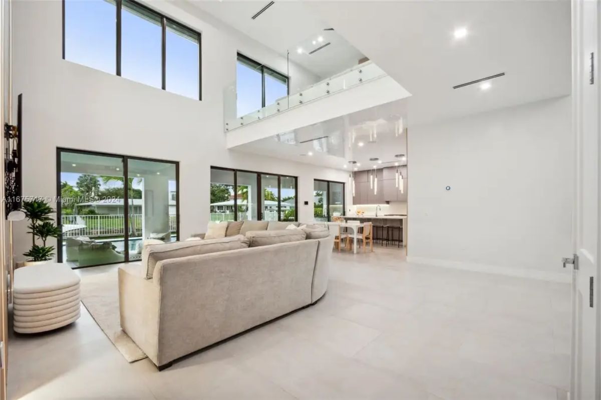 Open-concept living area with high ceilings, a neutral-colored sectional, and floor-to-ceiling windows allowing for plenty of natural light. 
