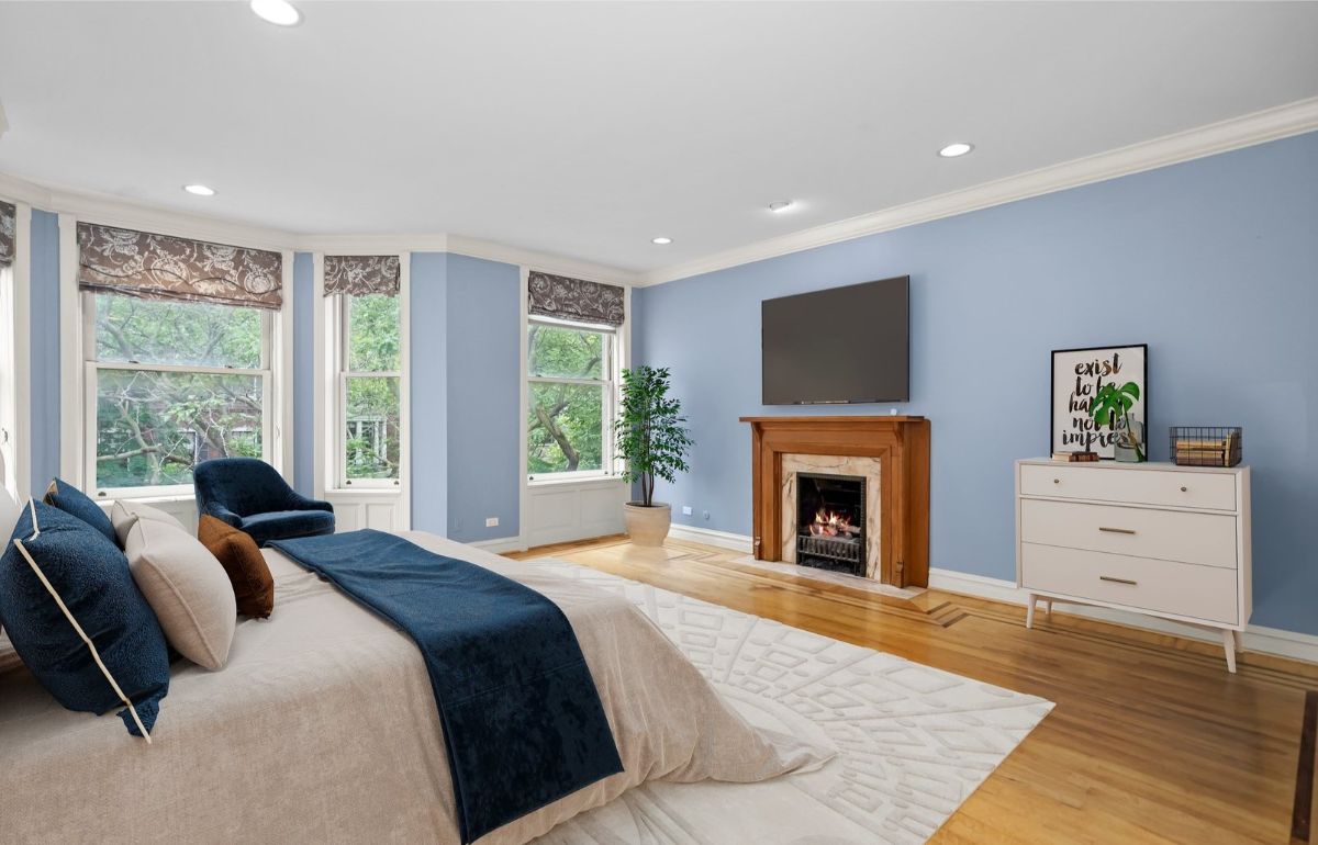 Soft blue walls contrast with warm wood flooring and a classic fireplace.
