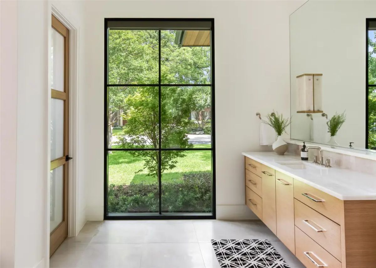 Bright and modern bathroom with a floating wooden vanity, large mirror, and a floor-to-ceiling window. 