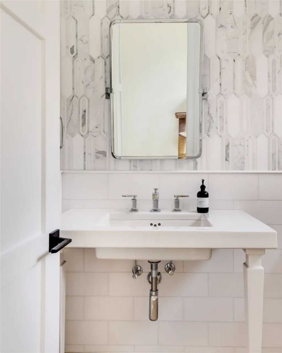 Small powder room with a white pedestal sink, geometric marble backsplash, and a vintage-style mirror. 