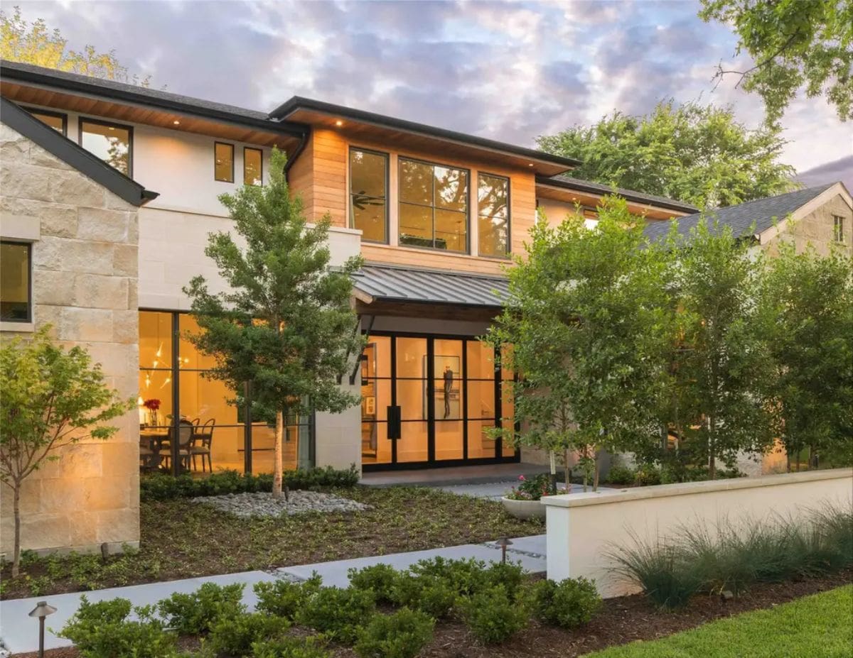 Warm and inviting front entrance with modern architectural details, lush greenery, and large glass windows. 
