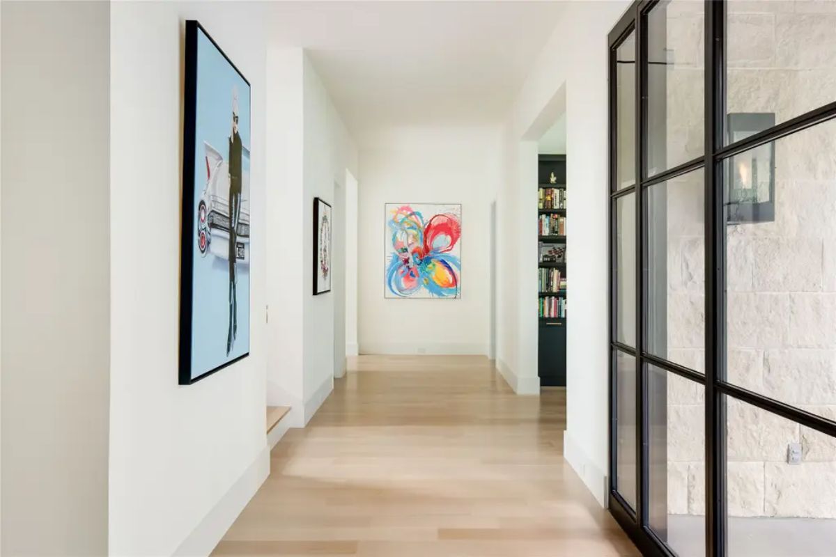 Minimalist hallway with light hardwood floors, modern artwork, and a glass partition. 