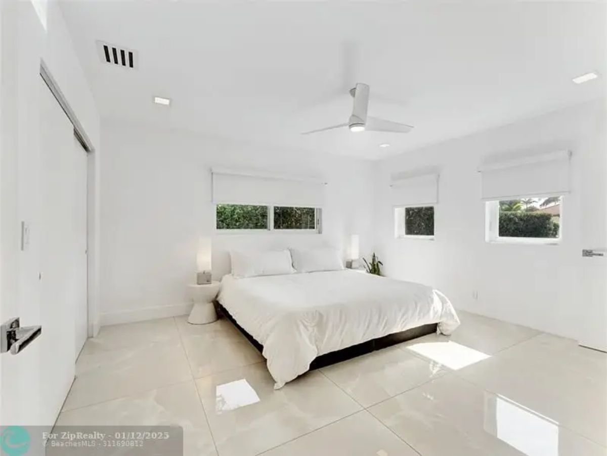 Minimalist bedroom with a white interior, large glossy tiles, and a ceiling fan. 