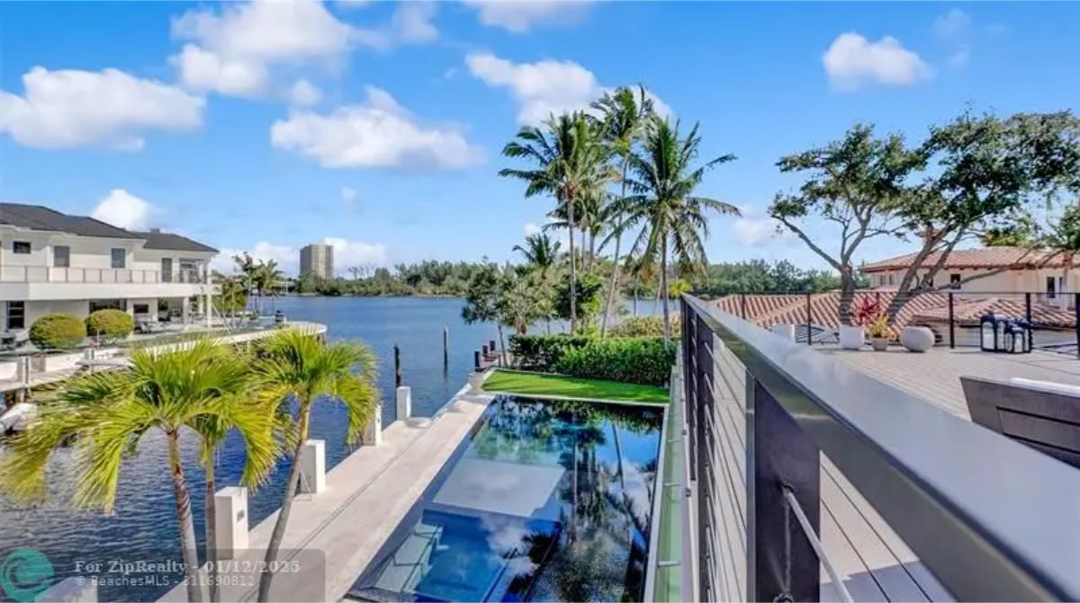 Waterfront view from the rooftop terrace overlooking palm trees, boats, and luxury homes. 