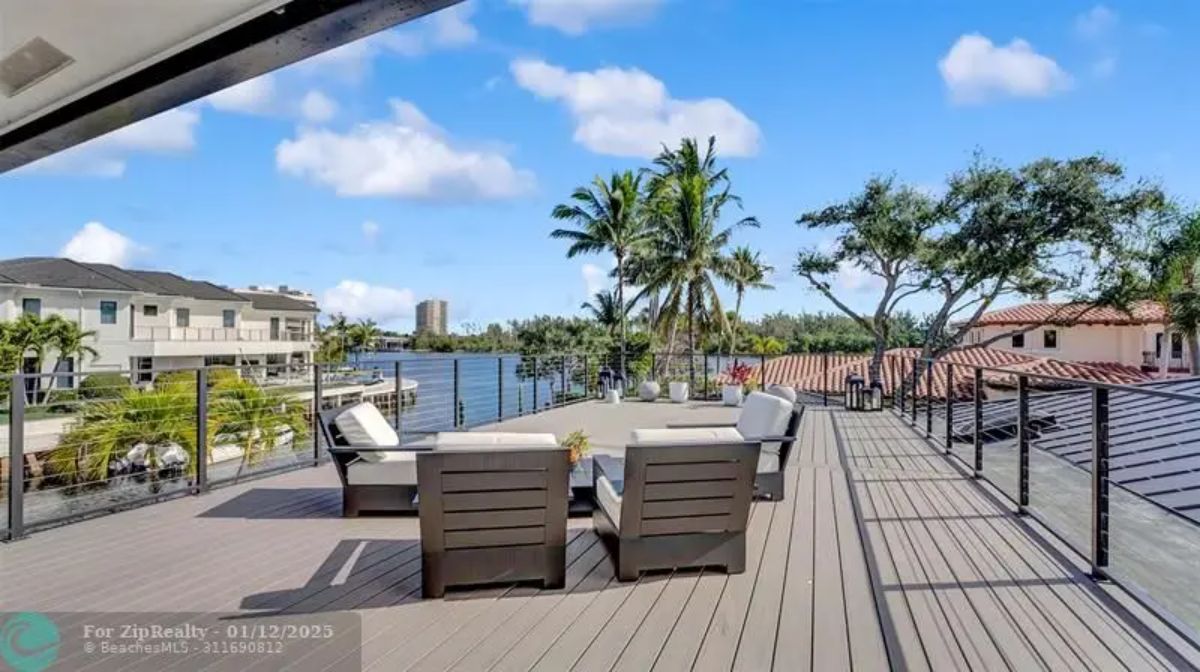 Rooftop terrace with lounge seating, a glass railing, and a panoramic water view. 