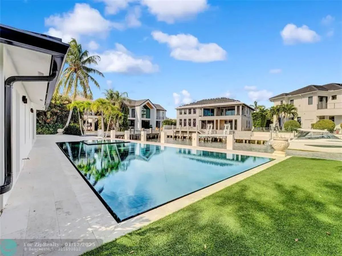 Infinity-edge pool with a green lawn, surrounded by waterfront properties and tropical landscaping. 
