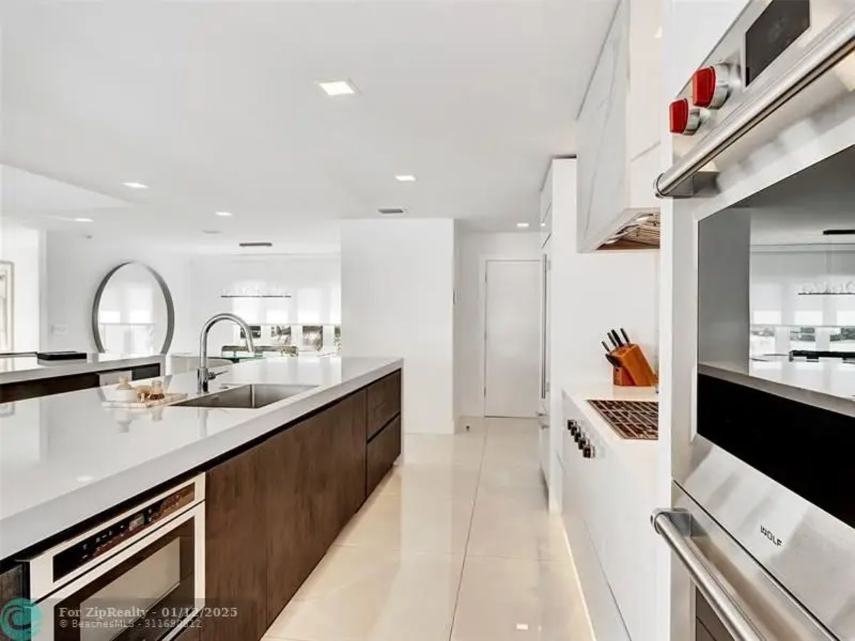 Sleek kitchen featuring built-in stainless steel appliances, white countertops, and wood accents. 