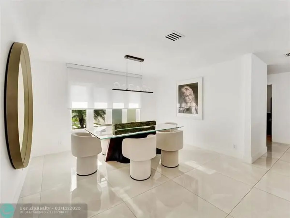 Chic dining space with a glass-top table, plush chairs, and a large artistic portrait. 