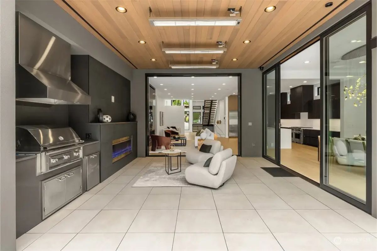 Open-concept indoor-outdoor living space with a built-in grill, fireplace, and contemporary seating. 