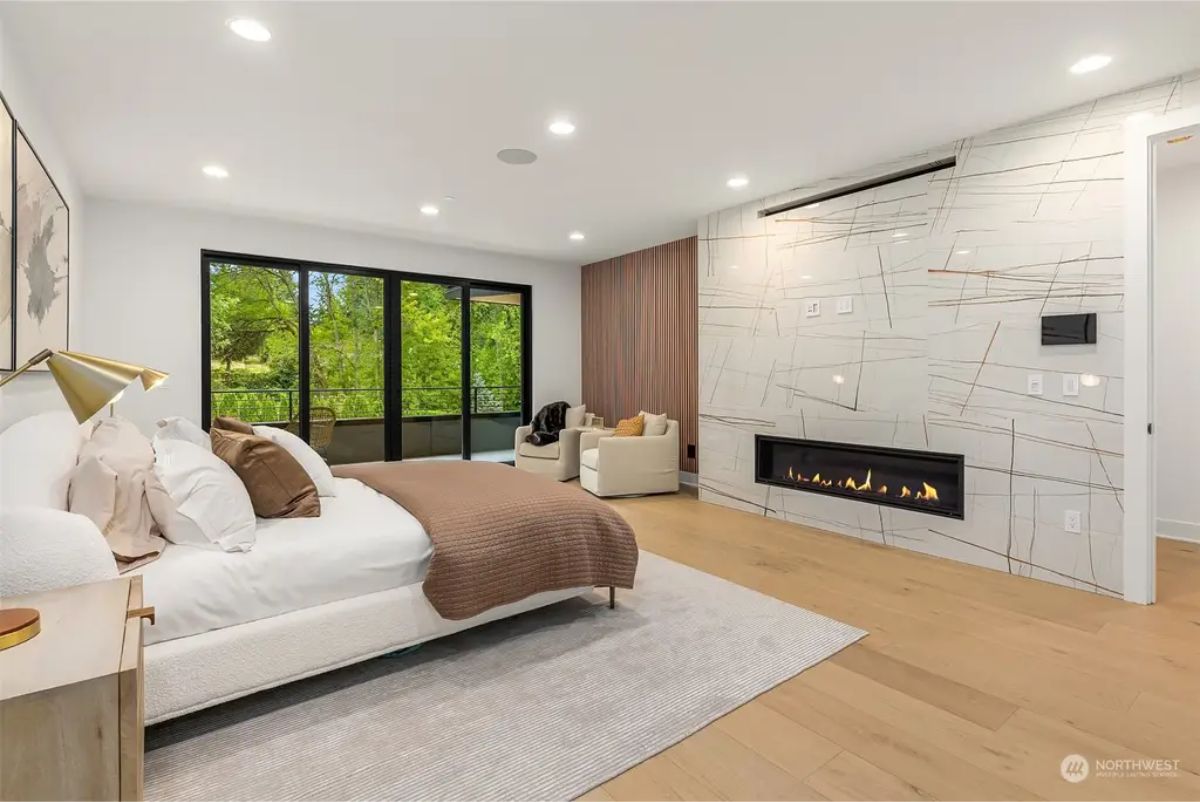 Luxurious bedroom with a marble-accented fireplace, soft neutral bedding, and floor-to-ceiling sliding doors leading to a private balcony. 