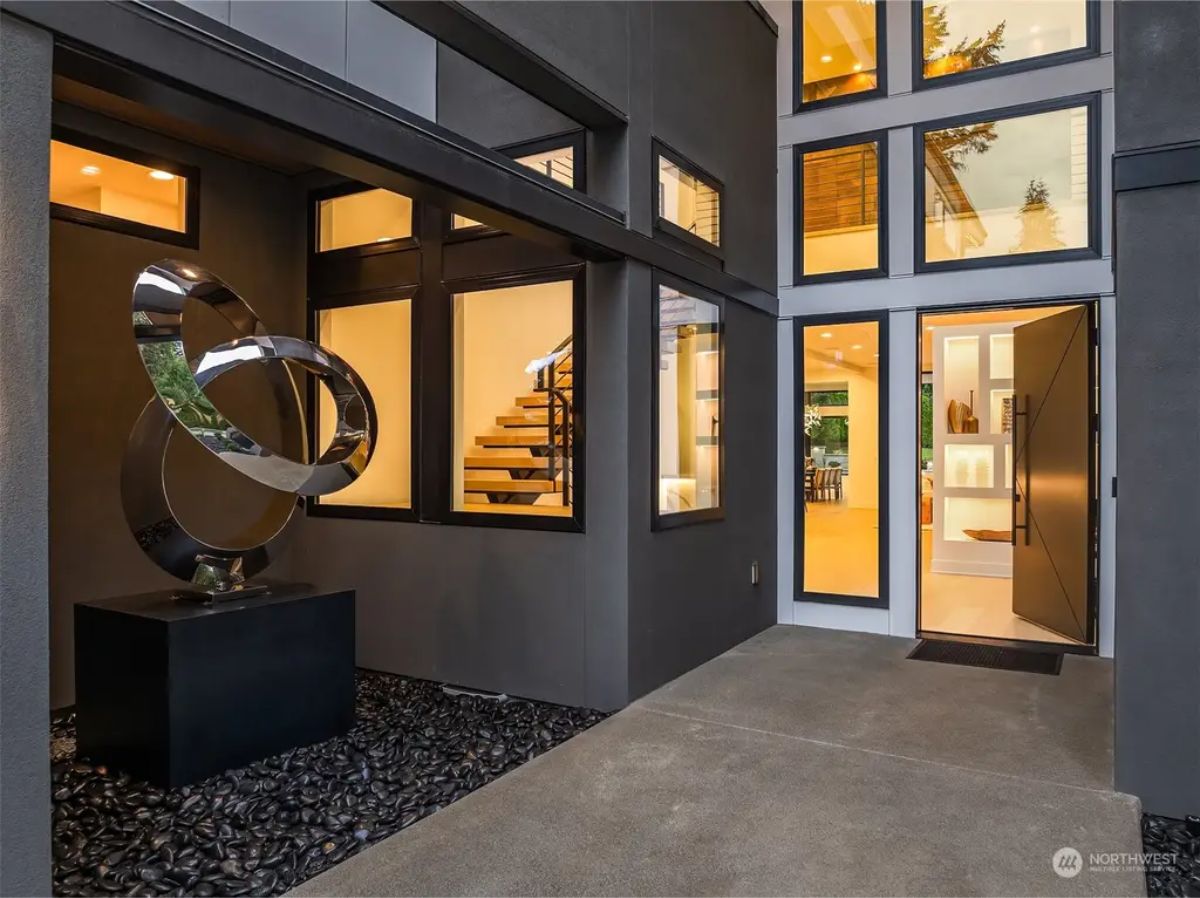 Entryway featuring a sleek black door, large windows, and a contemporary metal sculpture on a bed of black stones. 