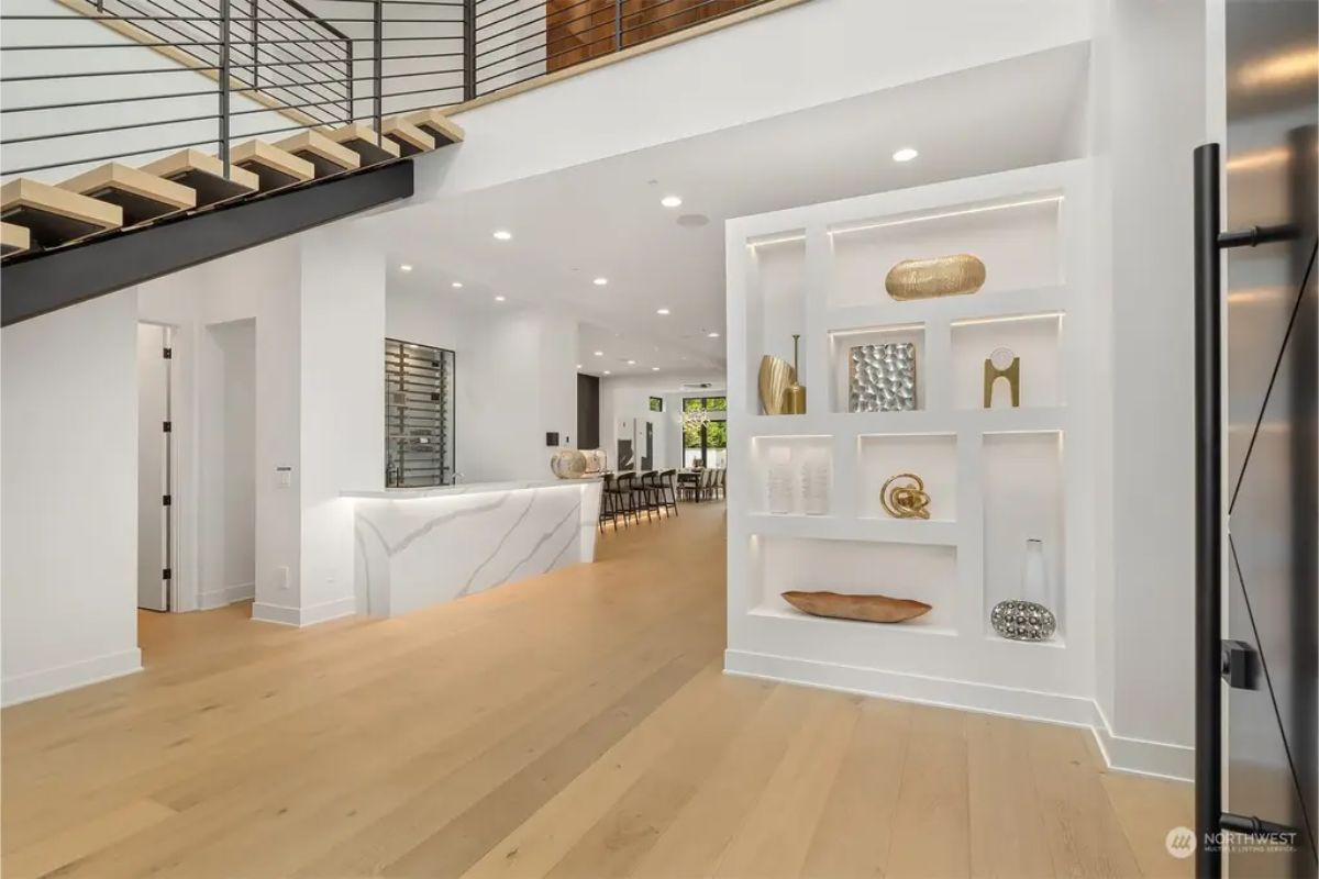 Open-concept living space with floating stairs, built-in shelving with warm lighting, and a sleek white marble bar. 