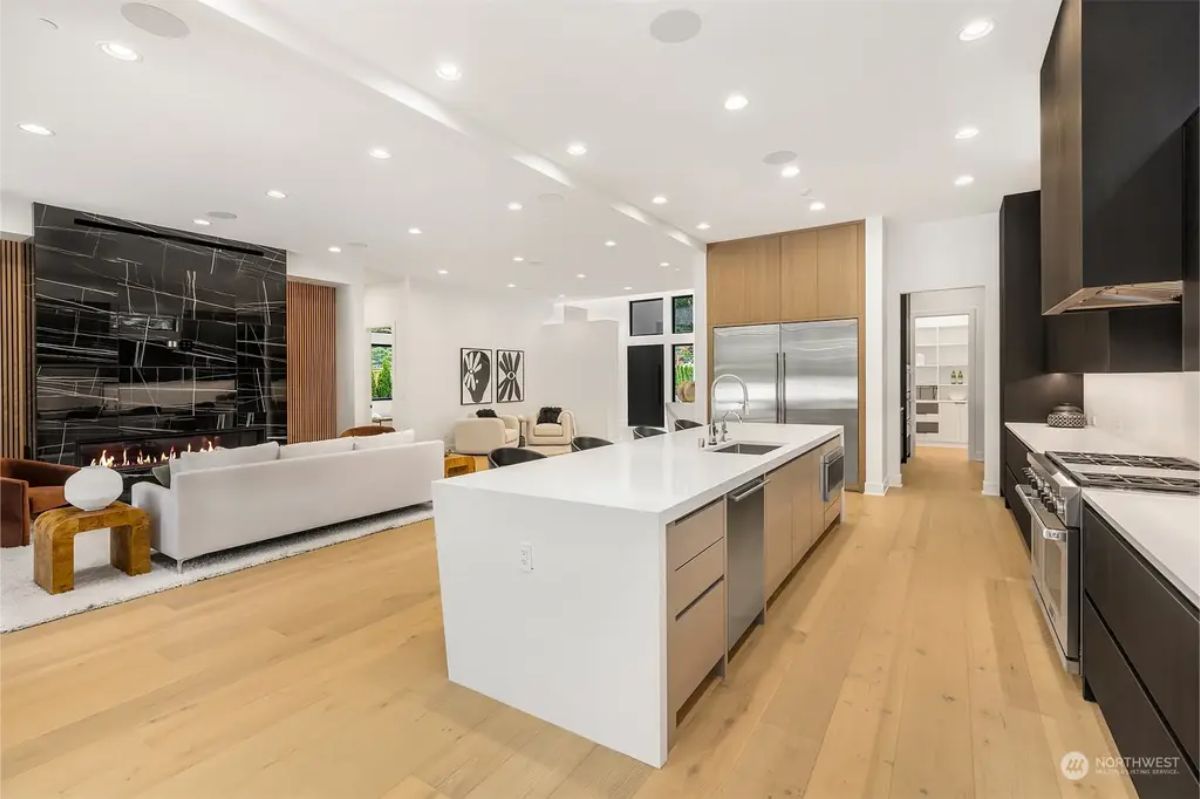 Expansive kitchen layout seamlessly connecting to the living area, featuring a white island, double refrigerators, and warm wood finishes. 