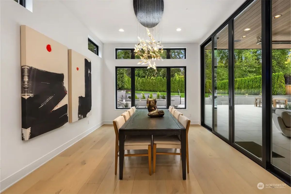 Elegant dining room with a black dining table, statement chandelier, and large sliding doors connecting to an outdoor patio. 