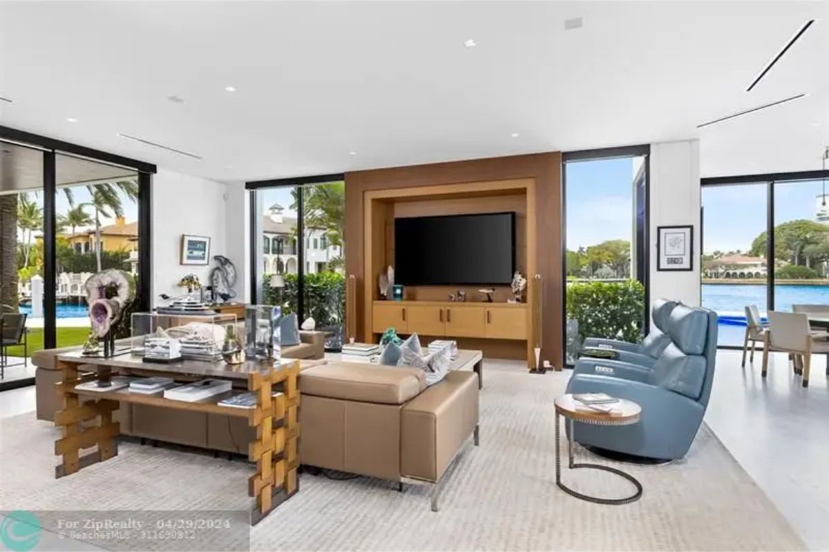 Bright family room with large windows, a mounted flat-screen TV, leather recliners, and views of the outdoor pool and water. 
