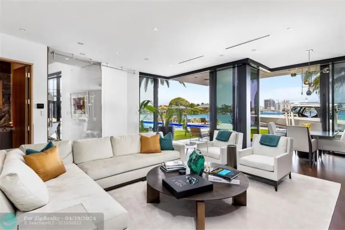 Cozy living space with light-colored sofas, accent pillows, a round coffee table, and views of the outdoor pool and marina. 