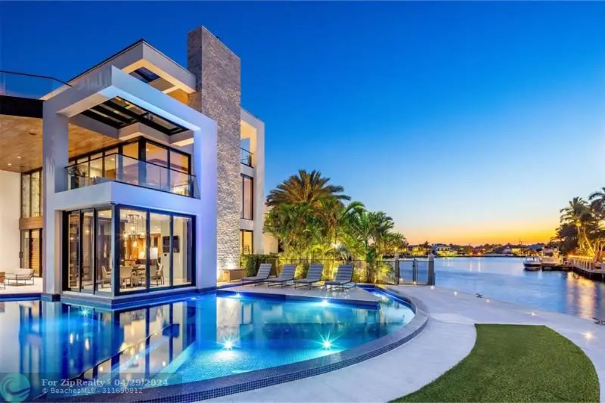 Curved swimming pool reflecting twilight hues with poolside chairs and waterfront views. 