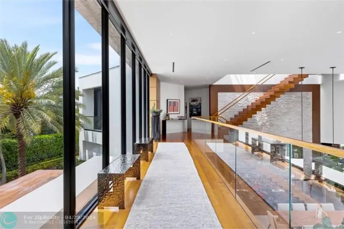 Upper floor hallway with glass railing and large windows overlooking palm trees. 