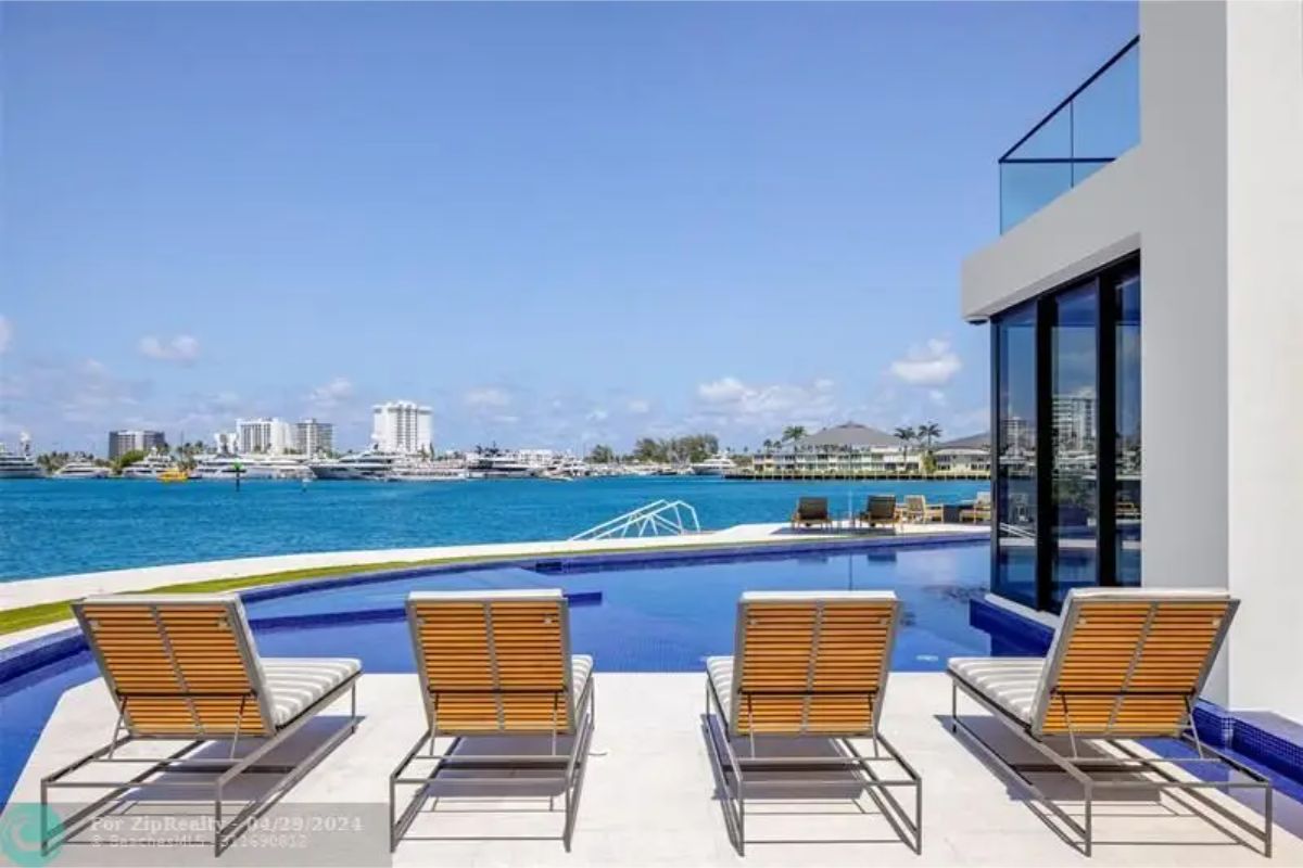 Poolside lounge chairs face a stunning waterfront with cityscape views in the distance. 