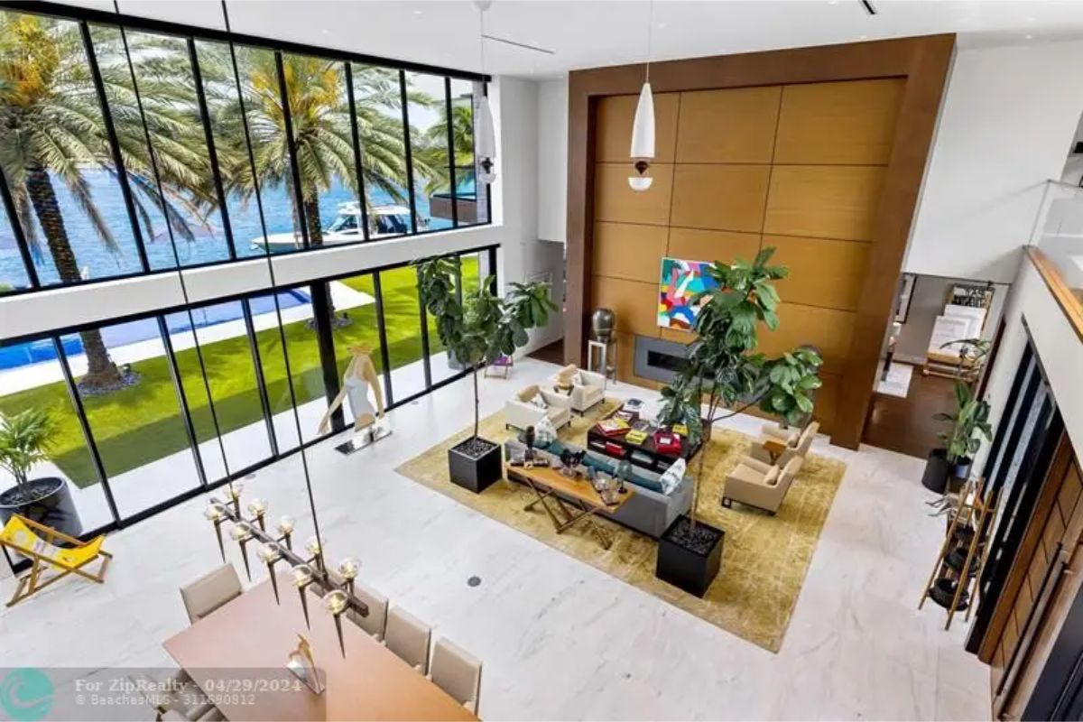 Open-concept living room with floor-to-ceiling windows, a tall wooden accent wall, modern furnishings, and indoor plants. 