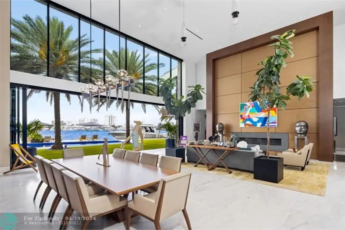 Open dining and living area with a long dining table, modern chandelier, large windows overlooking the water, and art decor. 