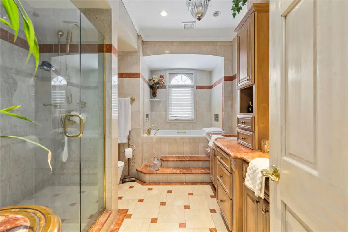 Spacious bathroom is designed with marble floors and countertops featuring gold and brown accents.