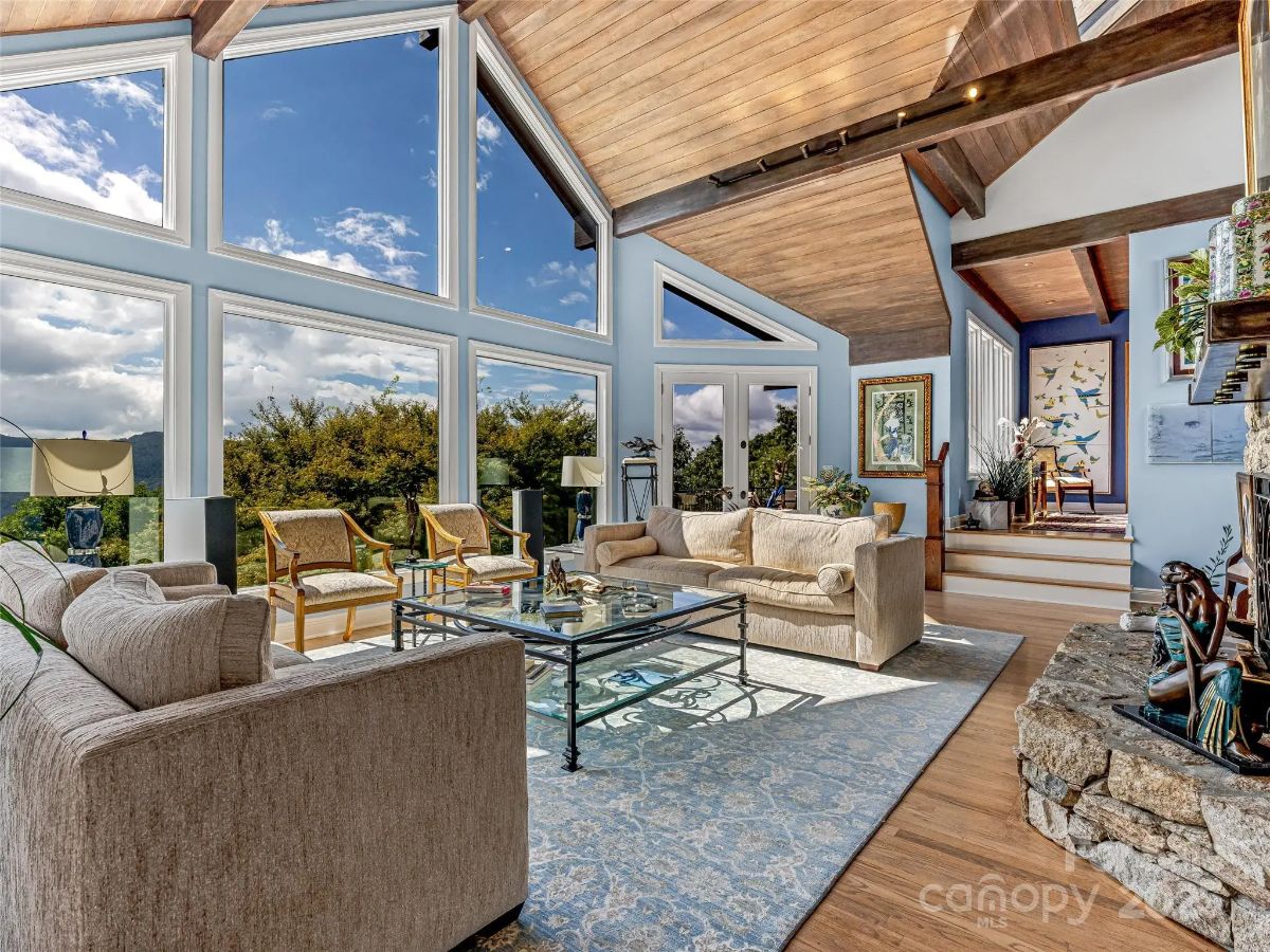 Large picture windows frame a view of trees and sky beyond the living room.