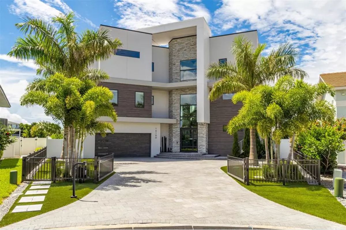 Driveway leads to a gated entrance with palm trees flanking both sides.