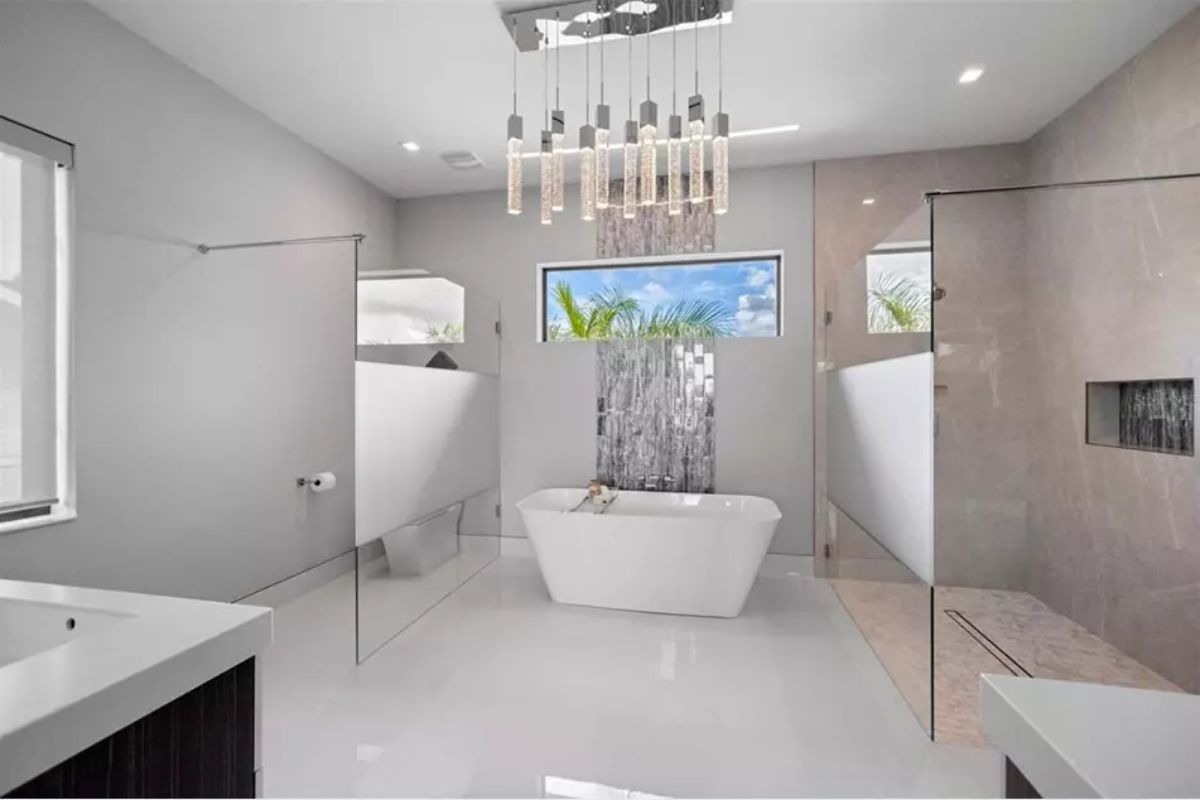 Bright bathroom with a central freestanding tub backed by a waterfall feature and wide landscape window.